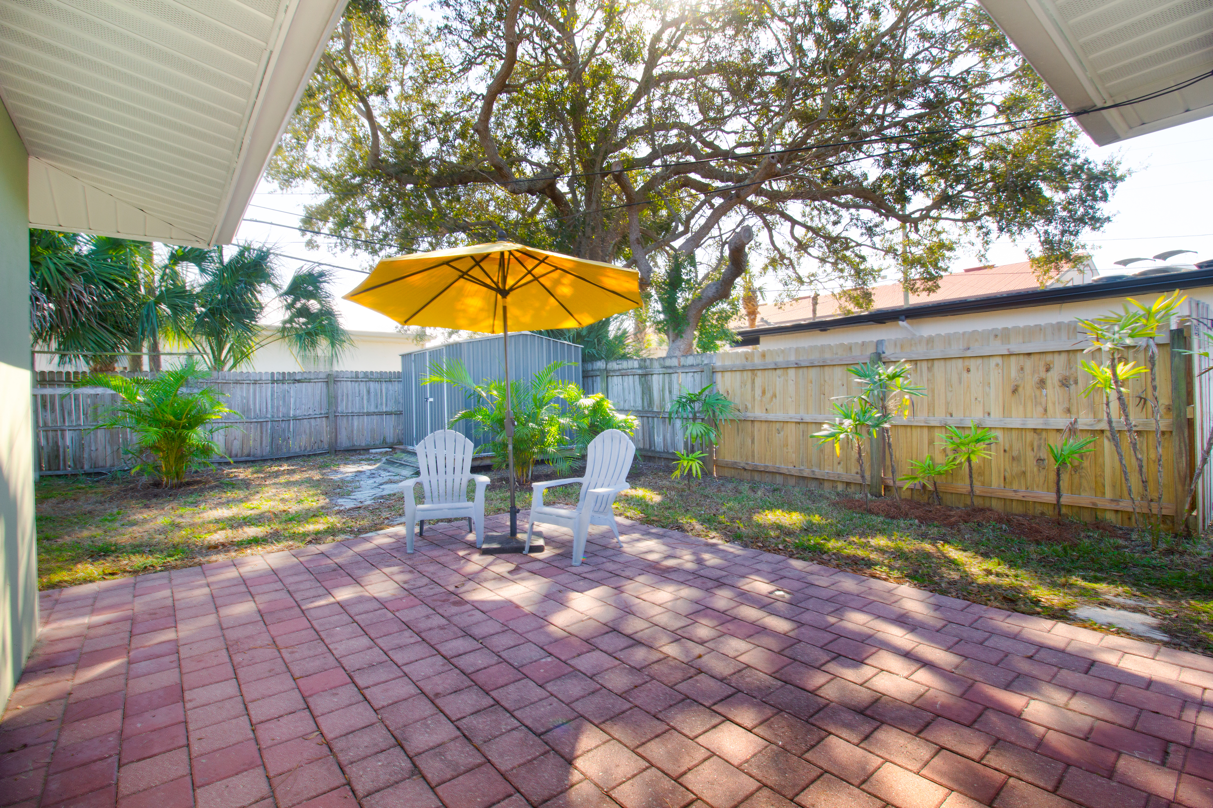 Brick patio with umbrella and two chairs and a tool shed in the corner